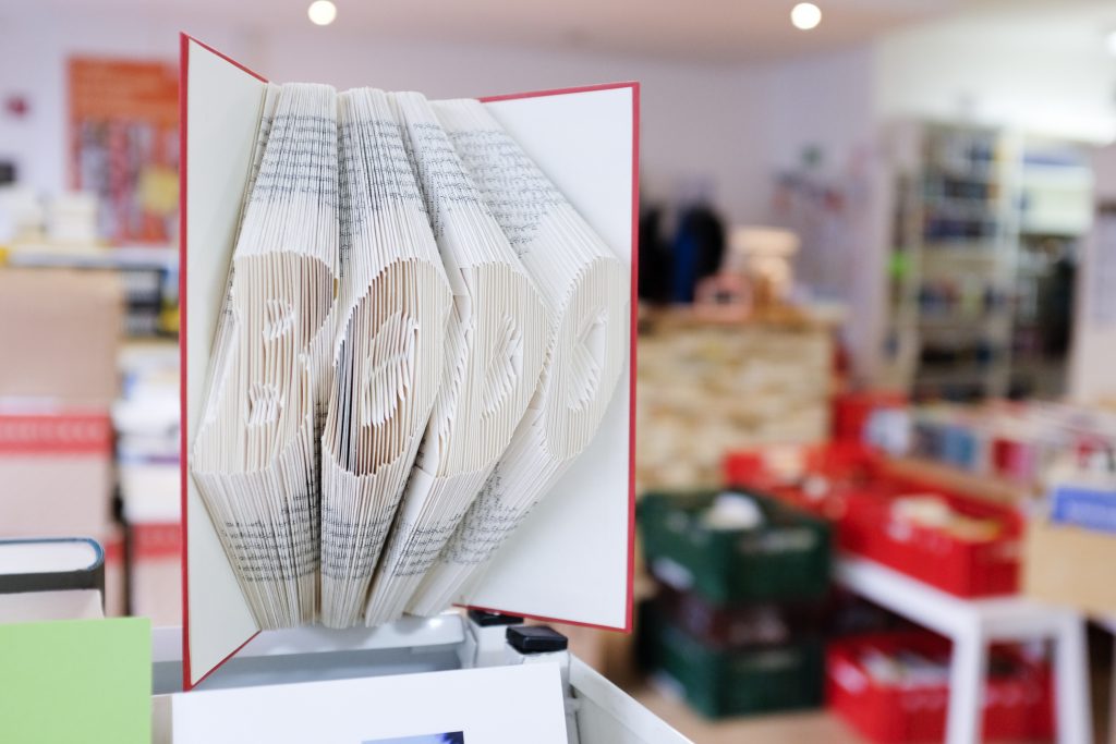 Ein Blick in den bodo-Buchladen. Im Vordergrund steht ein geöffnetes Buch, dessen Seiten kunstvoll gefaltet wurden. Die Faltung ergibt den Schriftzug "BODO".