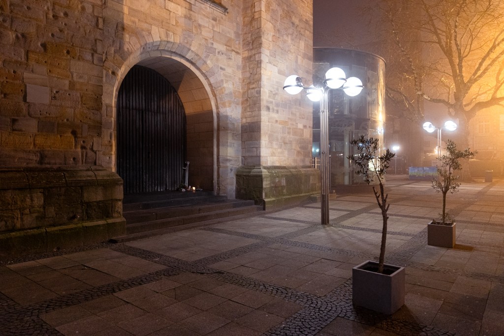 Die Seitentür der Reinoldikirche im abendlichen Nebel, daneben leuchten Straßenlaternen.
